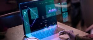 Person using a laptop with futuristic data dashboards and analytics visualizations projected in a virtual interface environment.