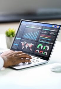 Person analyzing business performance data on a laptop screen showing charts, graphs, and global metrics in a modern dashboard.