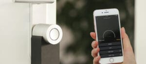 A person using a smartphone app to control a smart lock system, showing options to unlock, lock, and open a connected door remotely.