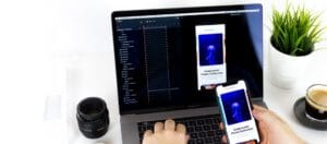 Designer testing underwater photo app UI on smartphone and MacBook, surrounded by camera lens, coffee, and green plant on desk.