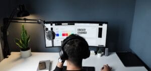 Man wearing headphones working on a curved monitor with design software, surrounded by desk accessories in a modern setup