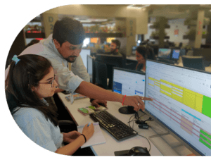 A software developer and quality analyst collaborate on a computer in a Top IT Company in India, focused on their work.