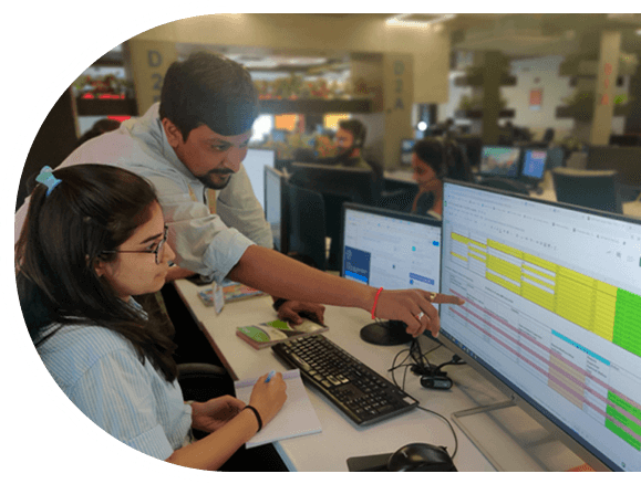 A software developer and quality analyst collaborate on a computer in a Top IT Company in India, focused on their work.